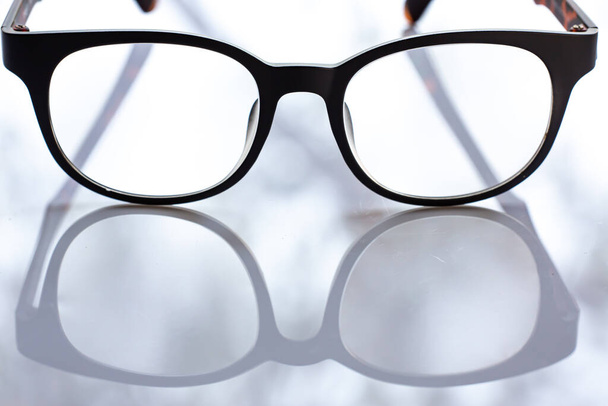 Black shortsighted or nearsighted eyeglasses on white acrylic table background, Close up & Macro shot, Selective focus, Reflection, Optical concept - Photo, Image