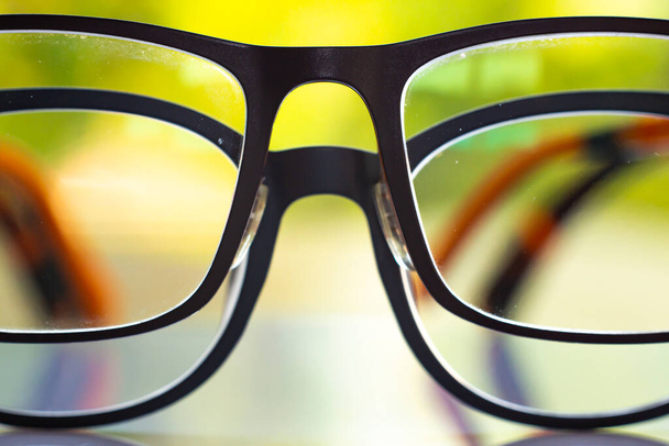 Two black shortsighted or nearsighted eyeglasses on white acrylic table, Bokeh green garden background, Close up & Macro shot, Selective focus, Reflection, Optical concept - Photo, Image