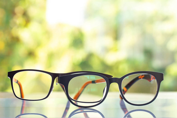 Two black shortsighted or nearsighted eyeglasses on white acrylic table, Bokeh green garden background, Close up & Macro shot, Selective focus, Reflection, Optical concept - Photo, Image