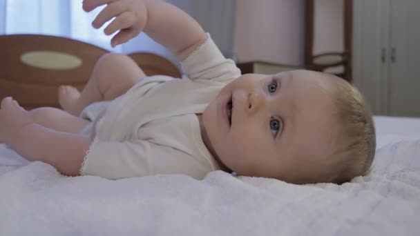 Cute baby with blue eyes lying on the bed - Footage, Video