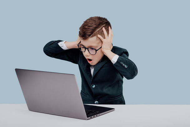 Stressed little entrepreneur using laptop blue background - Foto, afbeelding