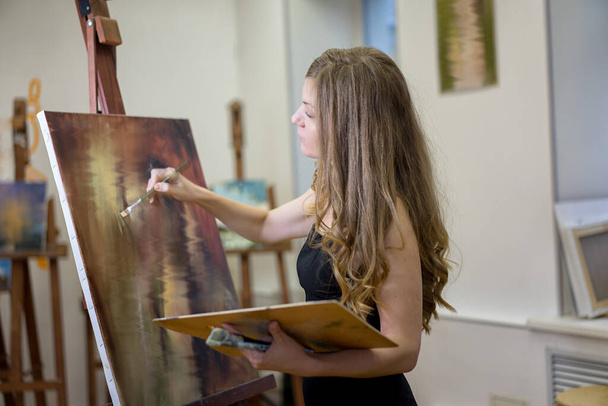 Vrouwelijke kunstenaar in kunststudio schildert een beeld, profielportret. Het beeld is wazig om onherkenbaar te worden. - Foto, afbeelding