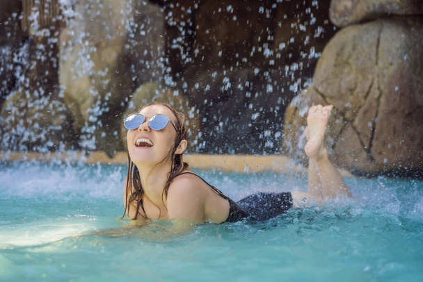 Junge fröhliche Frau unter dem Wasserstrom, Pool, Tagesbad, heiße Quellen - Foto, Bild