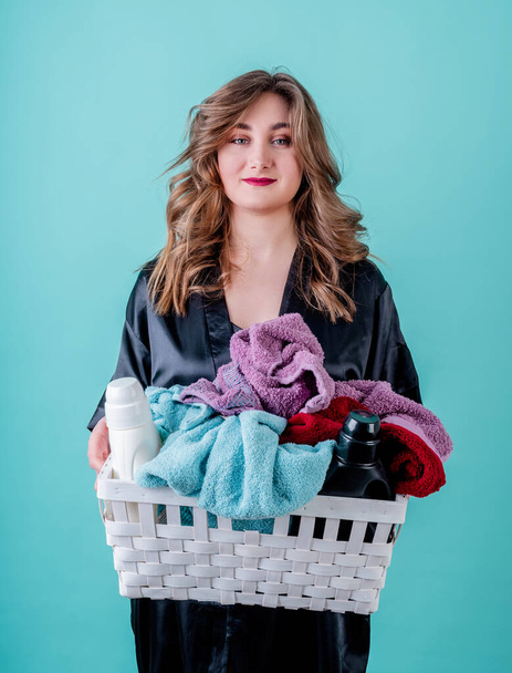 Conceito de lavandaria. Feliz dona de casa segurando uma cesta de roupas prontas para a roupa isolada no fundo azul
 - Foto, Imagem