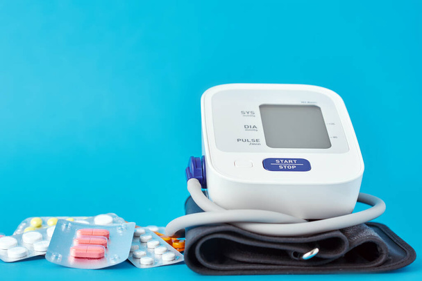 Digitale bloeddrukmeter en medische pillen op blauwe achtergrond. Begrip gezondheidszorg en geneeskunde - Foto, afbeelding