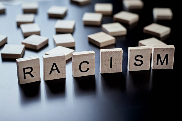 Rassismus und Missverständnisse zwischen Menschen, Vorurteile und Diskriminierung. Holzblock mit Wort Rassismus auf schwarzem Hintergrund - Foto, Bild