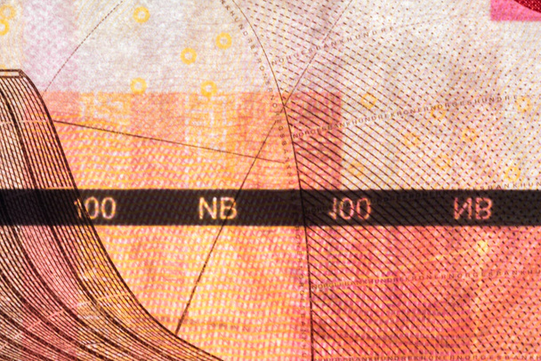 Пластиковая полоса безопасности внутри банкноты 100 норвежских крон. Полоса безопасности на банкноте норвежской кроны создана для предотвращения подделок
. - Фото, изображение