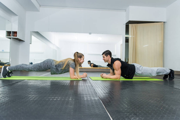 Kaksi ihmistä kuntosalilla tekemässä lankku liikuntaa yhdessä
 - Valokuva, kuva