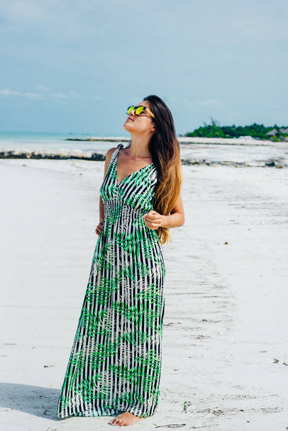красива дівчина в сонцезахисних окулярах в яскравій сукні на білому пляжі
. - Фото, зображення