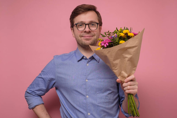 Jonge blanke man in blauw shirt en bril met bloemen als geschenk voor zijn moeder of vriendin - Foto, afbeelding