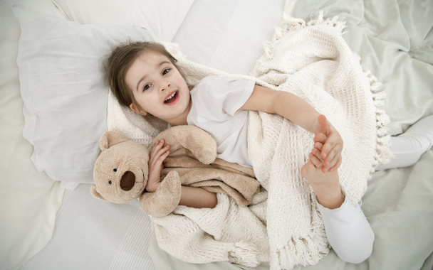 Sevimli küçük bir kız oyuncak bir ayıyla yatakta uyuyor. Çocuk gelişimi ve uyku kavramı. Yukarıdan görünüşü. - Fotoğraf, Görsel