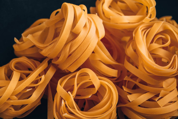 Pasta all 'uovo, Tagliatelle-Pasta, runde Kugeln roher Pasta auf schwarzem Hintergrund, Nahaufnahme einer rohen trockenen italienischen Pasta fettuccine auf schwarzer Tafel - Foto, Bild
