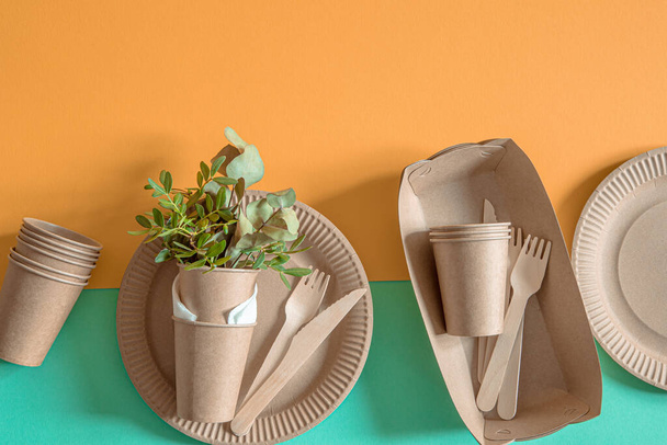 ECO craft paper tableware. Paper cups, plates, bag, fast food containers and wooden Cutlery with cornstarch on a colored orange-blue background. Recycling or the concept of zero waste. - Photo, Image