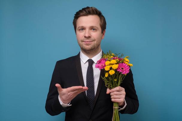 Jonge blanke man in pak met bloemen als geschenk voor vriendin aanzoek. - Foto, afbeelding