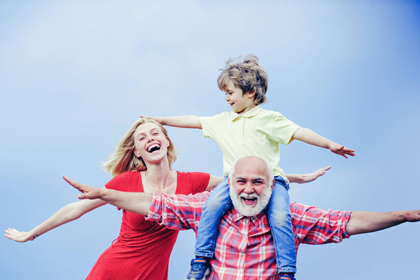 Bearded grandfather and grandson with mother playing with on sunny day. Grandson sits on the shoulders of his grandfather. Grandfather and grandchild. - Φωτογραφία, εικόνα