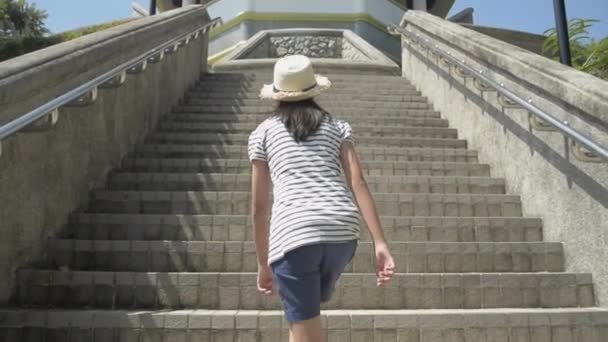 Aziatisch schattig meisje in casual jurk en het dragen van stro hoed lopen op de trap naar het uitkijkpunt toren. Volg slow motion shot van achteren. - Video