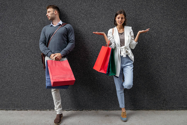 Γυναίκα και άντρας να κρατάνε τσάντες για ψώνια και να τσακώνονται για τα λεφτά. Καταναλωτισμός, πώληση, ζευγάρι, έννοια του στρες - Φωτογραφία, εικόνα