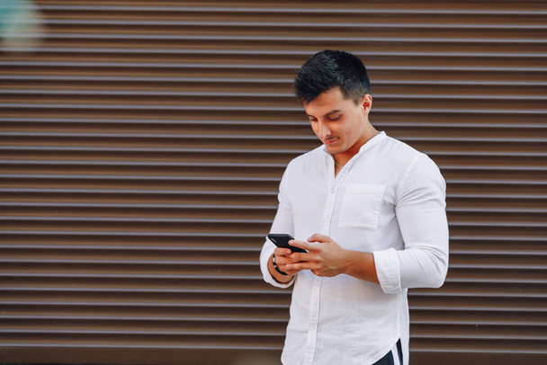 jeune gars élégant en chemise dactylographier sur le téléphone sur fond brun simple
 - Photo, image