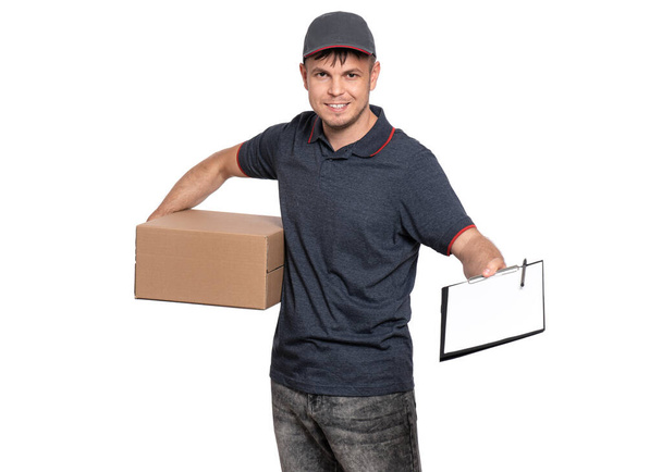 Portrait of Delivery man in cap holding cardboard box and clipboard with papers document. Handsome man, looking on camera. Courier isolated on white background. - Photo, image
