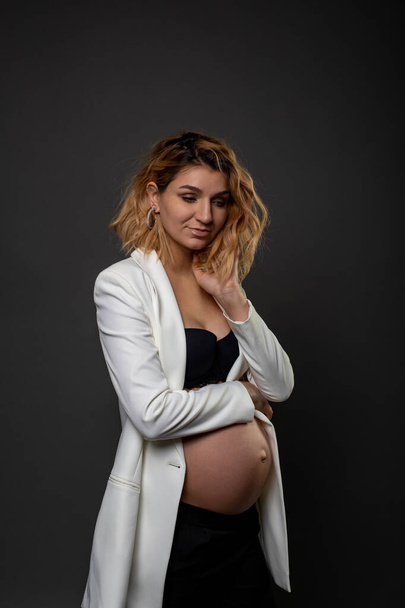 una hermosa mujer embarazada está de pie pensativa contra una pared negra
 - Foto, imagen