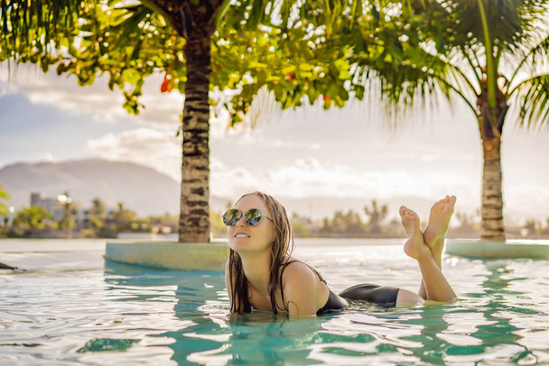 Luxury resort swimming pool. Beautiful woman tourist relaxing in holiday retreat on summer travel vacation. Bikini girl in sunbathing swimsuit enjoying ocean background - Photo, Image