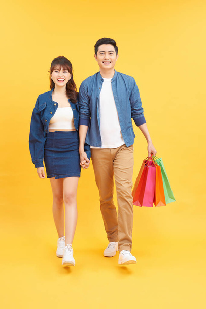 Asian couple shopping, full length portrait isolated on yellow background. - Fotografie, Obrázek