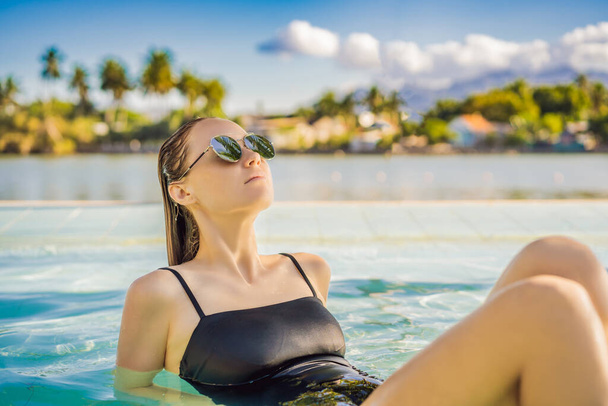 Luxury resort swimming pool. Beautiful woman tourist relaxing in holiday retreat on summer travel vacation. Bikini girl in sunbathing swimsuit enjoying ocean background - Фото, изображение