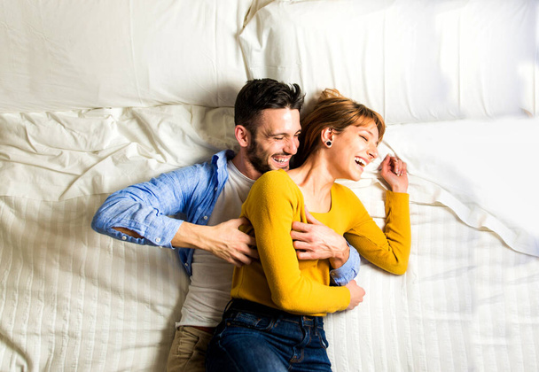 Two young adults at home - Beautiful happy couple of lovers having fun in bed - Foto, imagen