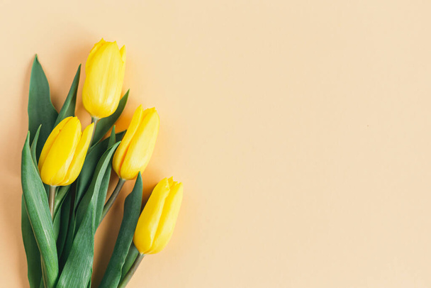 Gevoelige gele tulpen op pastelperzikondergrond. Wenskaart voor Moederdag. Plat gelegd. Plaats voor tekst.  - Foto, afbeelding