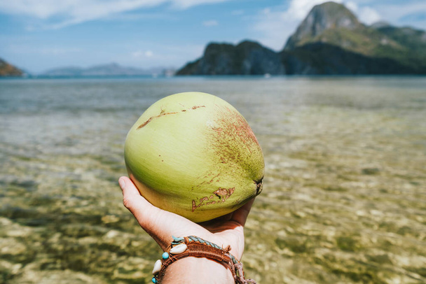 Close-up van kokosnoot in mannelijke handen tegen exotische oceaaneilanden - Foto, afbeelding