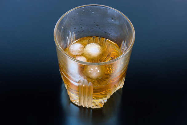 Стакан виски с кусочками льда на темной поверхности
 - Фото, изображение
