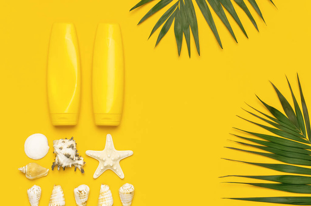 日焼け止めクリームの黄色のボトルは、熱帯のヤシの葉、シェル、黄色の背景にヒトデフラットレイアウトコピースペースを表示します。太陽の保護夏の背景休暇旅行のコンセプト夏の化粧品. - 写真・画像