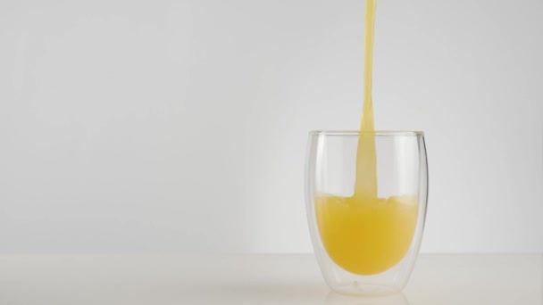 Fresh orange or pineapple juice is poured into a transparent glass with a double wall against light background. The concept of a healthy and clean food, diet, detox, vegetarian food. Wide shot - Imágenes, Vídeo