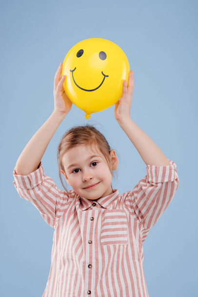 little girl holds up yellow balloon with smile. - Foto, immagini