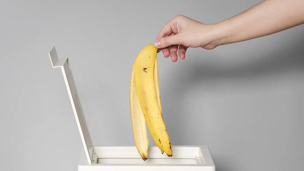 Hand puts banana peel in the bin for recycling.  - Fotografie, Obrázek
