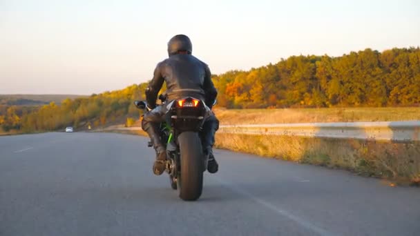 Nerozpoznatelný muž jedoucí na moderní sportovní motorce na podzimní dálnici. Motorkář závodní jeho motocykl na venkovské silnici. Motorkářská jízda na kole během cesty. Pojem svoboda a dobrodružství. Zadní pohled - Záběry, video