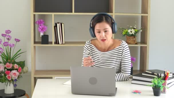 Vidéo de 4 ko de cours asiatiques en ligne avec casque d "écoute utilisant un ordinateur portatif et prenant des notes à la maison, éducation en ligne ou concept d'apprentissage en ligne - Séquence, vidéo