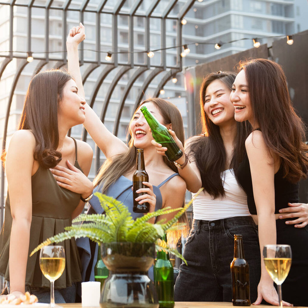 Ryhmä nuoria kauniita onnellisia aasialaisia naisia, joilla on pullo olutta chat yhdessä ystävien kanssa juhliessaan tanssijuhlaa ulkona katolla yökerho, jossa on kopiotilaa mainontaan
. - Valokuva, kuva