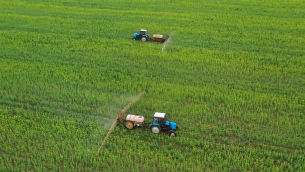 Aerial view of two tractors ride towards each other and spray fertilizer on agricultural plants on the rapeseed field - Footage, Video