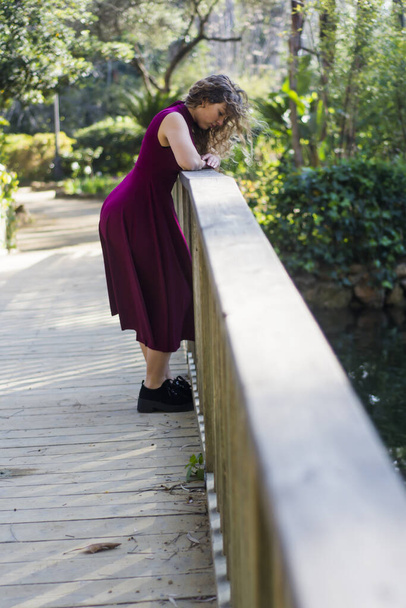 Mulher bonita em uma ponte de madeira no parque em um dia ensolarado
 - Foto, Imagem