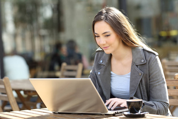 Young woman using her laptop sitting on a restaurant terrace a sunny day - Foto, imagen