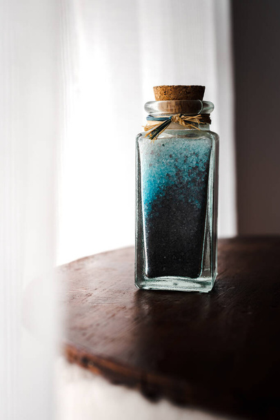 модная бутылка с солью для ванн голубого цвета для расслабляющих спа-процедур на белом фоне с естественным освещением
 - Фото, изображение