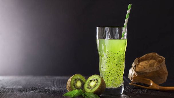 Fresh green vegan beverage in glass with straw with kiwi and basil seeds for health on black bachground with copy space, vegetarian food, dark key. Concept of natural coctail and juice. Detox. - 写真・画像