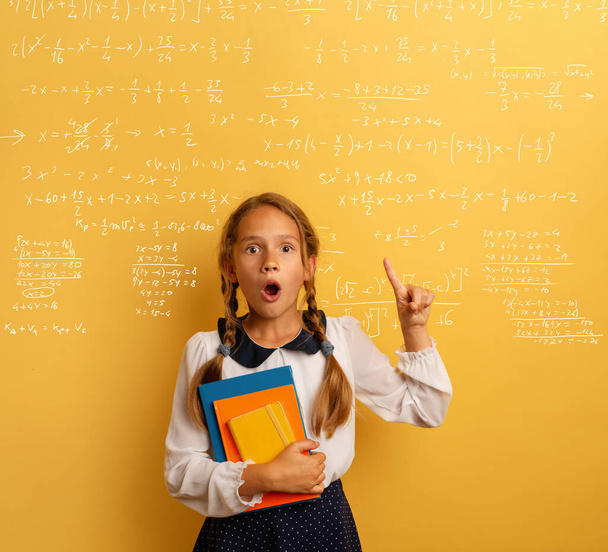 Young student is with shocked expression and indicates a complex formula. Yellow background - Fotoğraf, Görsel