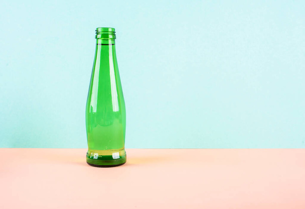 A glass water bottle is bright green on a light background. A place for text. - Photo, Image