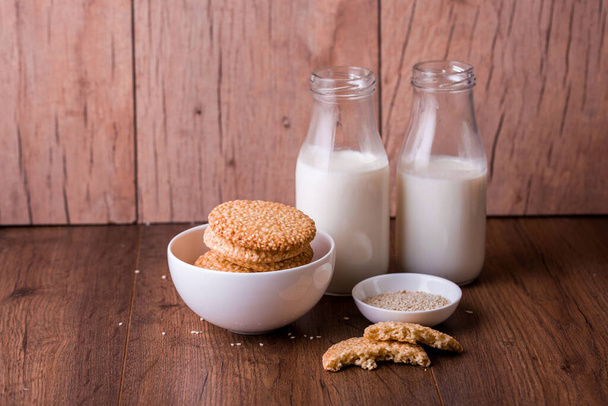 Biscuits ronds au sésame avec du lait et du jus sur la table. Graines de sésame pour la cuisson
 - Photo, image