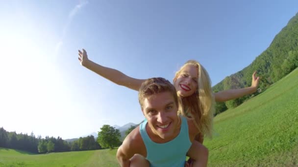 スローモーション:幸せな男は女の子にピギーバックライドを与えながら、カメラを見て. - 映像、動画