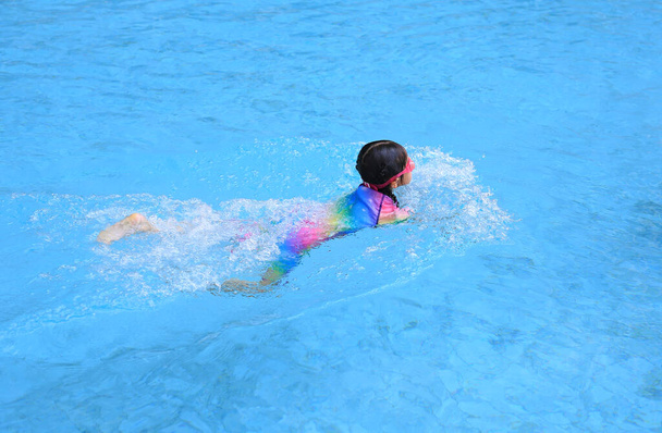 Ázsiai kislány, aki úszni tanul a medencében. Iskoláslány gyakorló úszás. - Fotó, kép