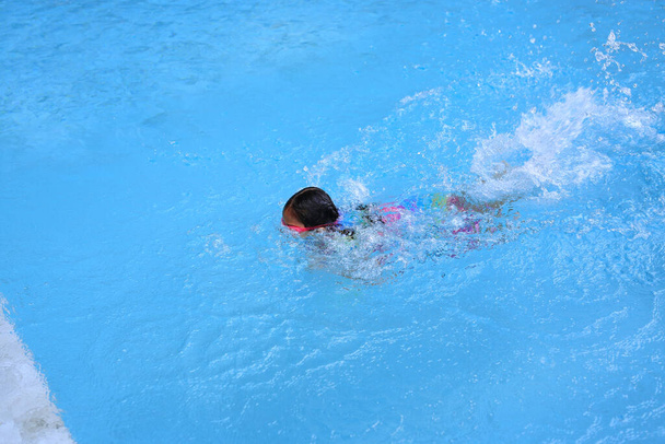 Asian little child girl learning to swim in pool. Schoolgirl practicing to swimming. - Фото, изображение