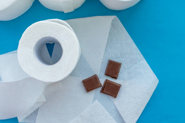 Concept. Chocolate on toilet paper next to a roll of toilet paper on a blue background. The view from the top. - Фото, изображение